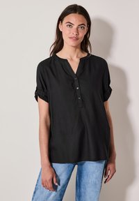 Sort skjorte med V-udskæring og opbrettede korte ærmer, lavet af et blødt stof, parret med lyseblå jeans.
