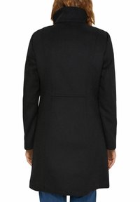 Manteau en laine noir avec un col montant, des détails de couture au dos et une coupe droite. Doté de manches longues et d'une longueur mi-cuisse.