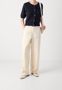 Navy short-sleeve cardigan with textured fabric and button front, paired with high-waisted cream wide-leg pants and beige flats.