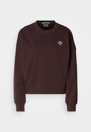 Crop top marrone realizzato in tessuto morbido, presenta un collo rotondo, polsini a costine e un piccolo logo ricamato blu sul petto.