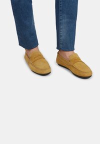 Žuti nubuk loafers sa mokućim šavovima i zaobljenim prstima, u paru s plavim ravnim trapericama. Mekana tekstura i nizak profil dizajna.