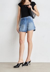 Svart figursydd topp, ljusblå denim kjolshorts med asymmetrisk fåll och knappstängning, kombinerat med svarta mules med klack.
