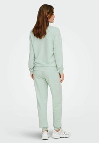 Mintgrønn bomullssweatshirt og matchende joggebukser, ribbede mansjetter, avslappet passform, brukt med hvite sneakers, sett fra baksiden.