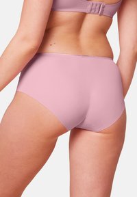 Slip in un delicato rosa chiaro con una texture liscia e design a piena copertura, caratterizzato da una leggera lucentezza lungo l'elastico in vita e le aperture per le gambe.