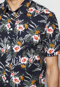 Kurzarmhemd aus navyfarbenem Stoff mit einem floralen Muster aus weißen und roten Blumen, grünen Blättern und orangefarbenen Akzenten. Mit Knopfleiste.