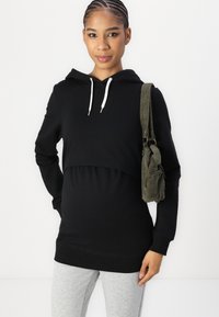 Black cropped hoodie made of soft material, featuring a drawstring hood and paired with gray leggings, accessorized with a green corduroy bag.