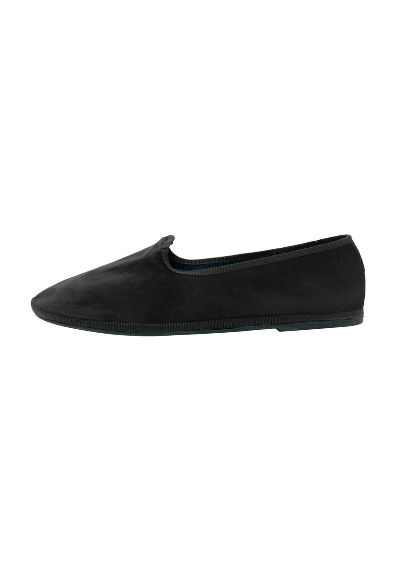 Zapato negro de ante tipo slip-on con punta afilada y diseño minimalista. Presenta un ribete elástico alrededor de la abertura y una suela de goma flexible.