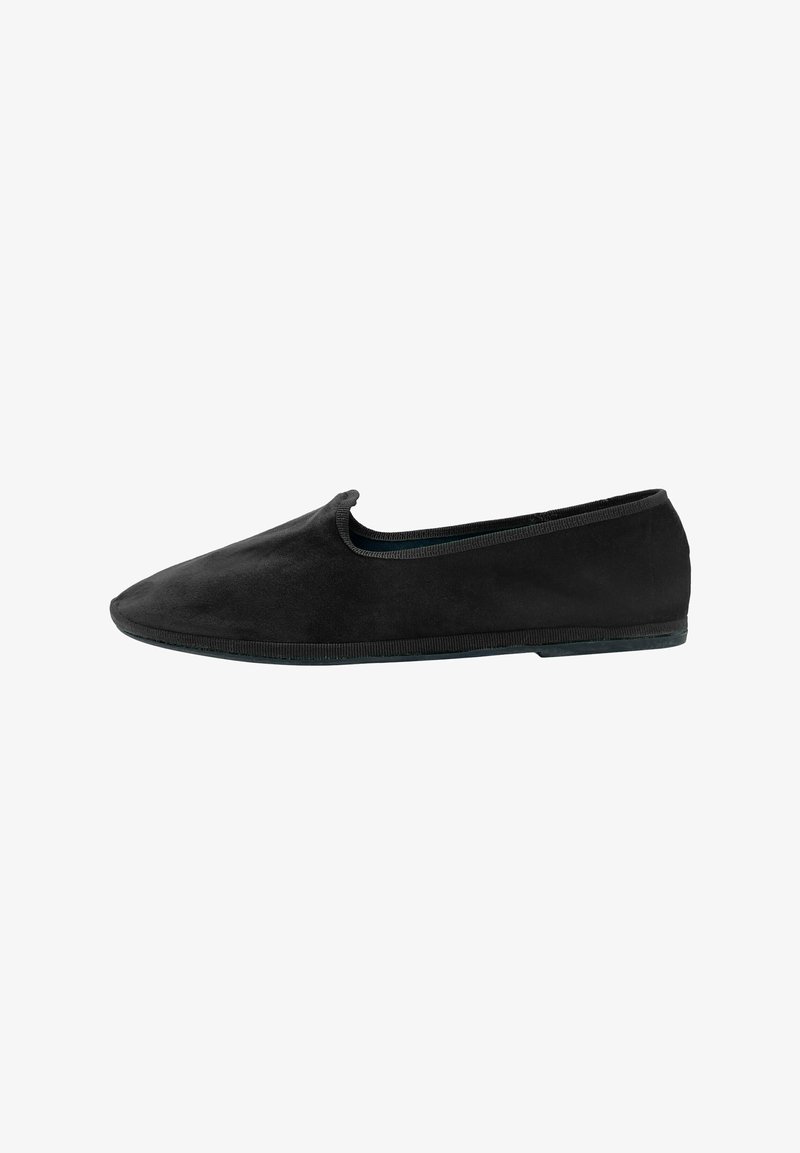 Zapato negro de ante tipo slip-on con punta afilada y diseño minimalista. Presenta un ribete elástico alrededor de la abertura y una suela de goma flexible.
