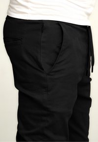 Black jogger pants made of smooth fabric, featuring side pockets and drawstring. Detailed stitching adds texture to the design.