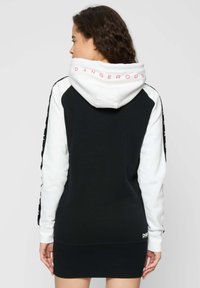 Sudadera con capucha en blanco y negro con un diseño contrastante, que presenta el texto "DANGEROUS" en la capucha y franjas laterales. Textura de tela suave.