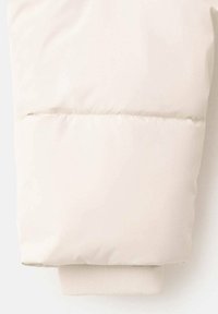 Beżowy rękaw pikowanej kurtki z poziomym przeszyciem oraz beżowym ściągaczem z dzianiny prążkowanej, nieco wystającym z końca rękawa.