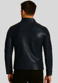 Marineblaue Lederjacke mit minimalistischer Gestaltung, die eine glatte Textur, strukturierte Schultern und subtile Nähte auf dem Rücken aufweist.