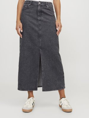 Black denim maxi skirt with a front slit, featuring a high waist, five pockets, and contrast stitching details. Paired with white sneakers.
