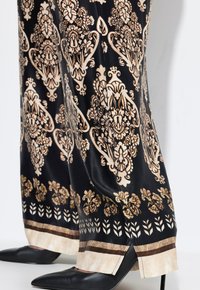 Zwarte gebloemde broek met gouden en crèmekleurige bloemmotieven, met een brede zoom en zijsplitten. Gecombineerd met elegante zwarte pumps.