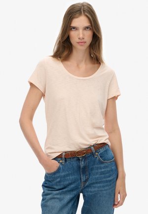 Camiseta de manga corta en color durazno claro con cuello redondo, hecha de un tejido suave, combinada con jeans de denim azul de cintura alta y un cinturón trenzado marrón.