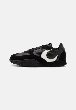 Schwarze Sneaker mit einem Obermaterial aus glattem Leder und strukturiertem Wildleder, weißem Akzentlogo, schwarzer Sohle mit kreisförmigem Profil.