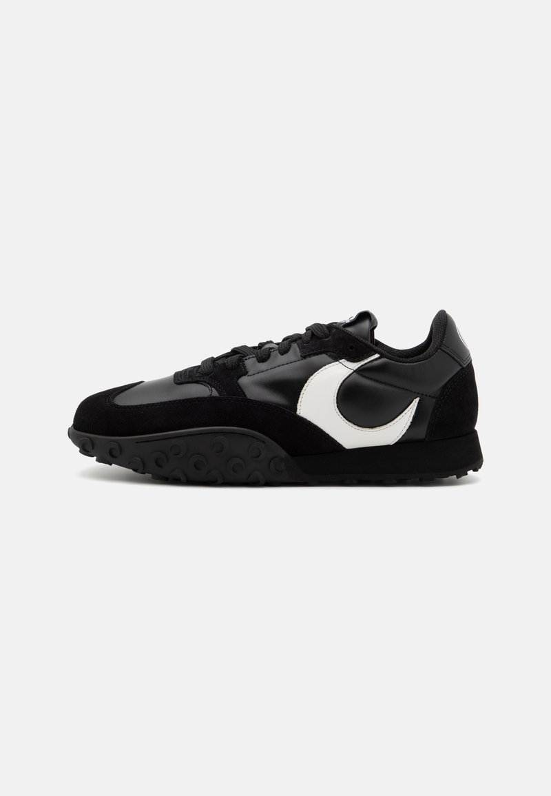Svart sneakers med en slät läder och texturerad mocka ovandel, vit logotyp i accentfärg, svart sula med cirkulärt mönster.