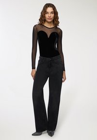 Body nero di velluto con maniche lunghe in rete trasparente, scollatura a forma di cuore; abbinato a jeans neri a vita alta e gamba larga e tacchi metallici.
