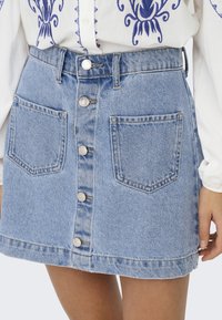 Light blue denim skirt with a button-front closure, two front pockets, and a frayed hem. Material is sturdy, with a smooth, textured finish.