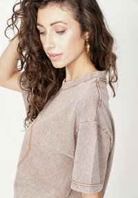 Przesadnie duży t-shirt w kolorze taupe wykonany z miękkiej tkaniny, wyposażony w prążkowany kołnierzyk, krótkie rękawy oraz subtelne kontrastowe przeszycia.