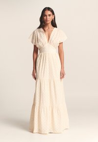 Maxikjole i creme med struktureret stof. Har dyb V-hals, flagrende ærmer og lagdelt kant. Enkel og elegant design.