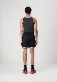 Shorts de sport noirs avec des bordures blanches, débardeur gris et chaussures à semelles rouges. Tissu lisse avec une coupe ample. Vue de l'arrière.