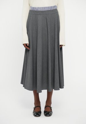 Gray pleated skirt made of textured fabric, featuring a contrasting waistband. Paired with black shoes with decorative accents.