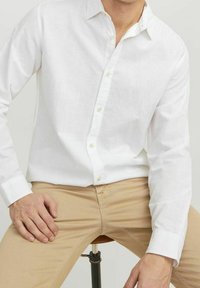 Camicia bianca in lino con maniche lunghe, dotata di un colletto classico e pantaloni leggeri color beige. Tessuto morbido, design semplice e materiale leggero.