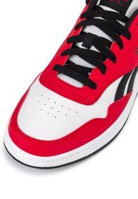 Punane ja valge sportlik jalanõud, millel on sile nahk ülemine osa, mustad paelad, pehmendatud keel ja perforatsioonid varbaküljel hingavuse tagamiseks.