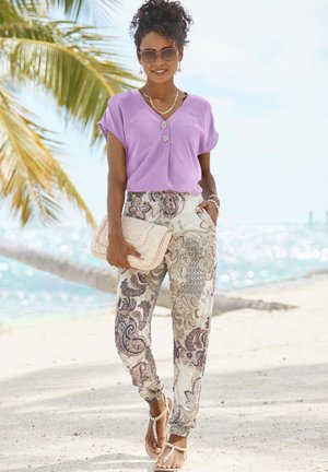 Paarse korte mouwen blouse met knopen, geprinte beige jogpants met zijzakken en tan sandalen, aangevuld met een gevlochten handtas en accessoires.