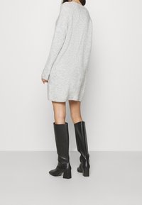 Abito maglione grigio chiaro a coste con maniche lunghe e una vestibilità comoda, abbinato a stivali neri in pelle con tacco al ginocchio.