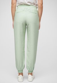 Jogging en tissu vert clair avec une taille élastique, deux poches arrière et des poignets élastiques aux chevilles. Associé à des baskets blanches.