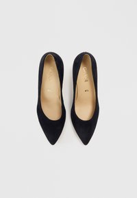 Sorte semskede pumps med spiss tupp, glatt tekstur og beige innvendig fôr. Har subtil merking og et slankt design. Størrelse 4,5.