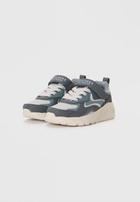 Sportliche Sneaker mit oberen Teilen in Dunkelblau und Hellblau, weißen Schnürsenkeln und einer dicken, hellbeigen Sohle. Mit einem Klettverschluss-Riemen oben.