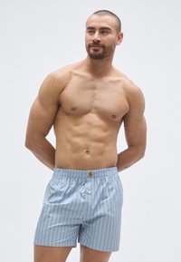 Világoskék csíkos rövidnadrág, gumis derékrésszel és gombos záródással. Az anyag sima, függőleges fehér csíkokkal és logó címkével.