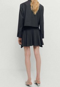 Dark gray cropped blazer paired with a flared skirt. The blazer has long sleeves and buttons, while the skirt features a soft, pleated texture.
