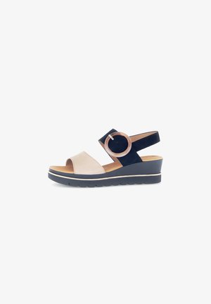 Beige and navy wedge sandals with a wide strap and circular accent. Soft material, open toe design, and textured sole for grip.