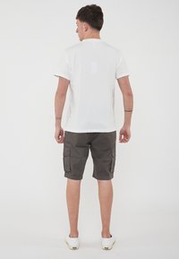T-shirt bianca a maniche corte con scollo a giro, abbinata a pantaloni cargo grigio scuro con tasche laterali, indossata con scarpe bianche slip-on.