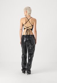 Haut court noir avec des bretelles croisées dans le dos, associé à un pantalon noir brillant orné de sequins. Silhouette slim et jambe fuselée.