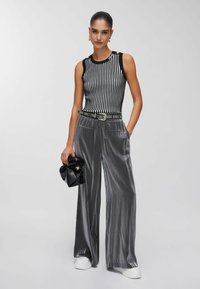 Haut sans manches à rayures verticales noires et blanches, associé à un pantalon large en satin gris taille haute, souligné par une ceinture cloutée et un sac à main.