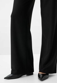 Svarta vida byxor i slät tyg, kombinerat med svarta skor med spetsig tå och låg klack. Ren, minimalistisk design.