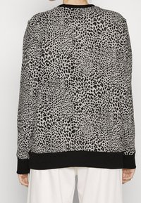 Persona vistiendo un suéter de cuello redondo de manga larga con estampado de animal en blanco y negro y puños y dobladillo negros, combinado con pantalones blancos.