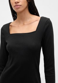 Svart langermet topp med firkantet halsutringning og mykt, teksturert stoff. Tettsittende silhuett med minimalt med detaljer.