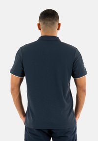 Polo de color náutico hecho de tejido texturizado, con un cuello clásico, mangas cortas y acentos blancos en los puños de las mangas y el cuello.