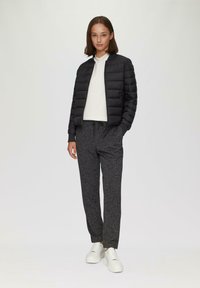 Czarna puchowa kurtka z zapięciem na zamek, biała sweter z okrągłym dekoltem, szare dresowe spodnie w wzory oraz białe sneakersy na platformie.