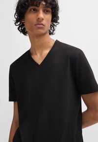 Tricou negru cu decolteu în V, fabricat dintr-un material moale și ușor, cu mâneci scurte și croială lejeră. Design minimalist; fără modele sau logo-uri vizibile.