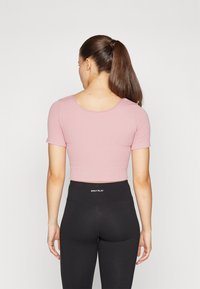 Top corto rosa con mangas cortas y textura acanalada. Combinado con leggings negros de talle alto que presentan un logo en la cintura.