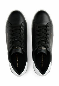 Schwarze Leder-Low-Top-Sneaker mit weißen Fersenakzenten, schwarzen Schnürsenkeln und goldfarbenem Tommy Hilfiger-Branding an den Seiten und auf den Innensohlen.