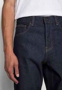 Donkerdenim jeans met gele stiksels, recht ontwerp, voorkantzakken en een knoopsluiting. Het materiaal lijkt stevig met een gladde textuur.