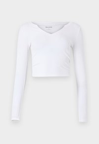 Bijela dugokrilna crop majica od rebrastog materijala. Ima V-izrez i uski kroj. Minimalistički dizajn bez vidljivih ukrasa.